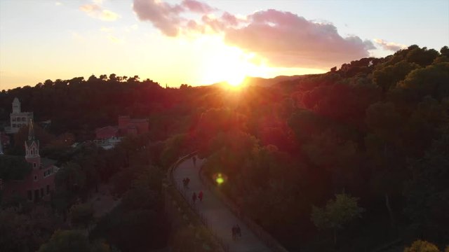 drone overflies the famous viaduct in parc guell in Barcelona during the sunset with sun-flares during golden hour