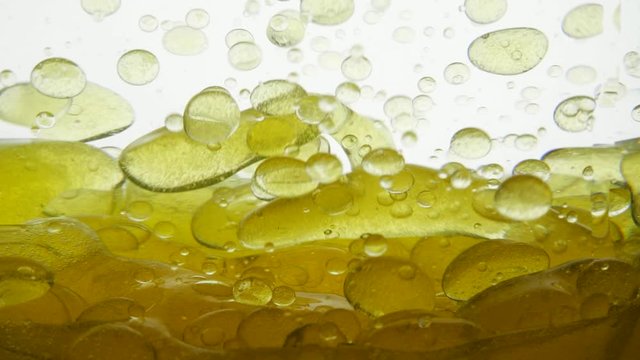 Beautiful grape seed oil settles on the surface of a white background liquid. Fragrant and tasty walnut oil flows around the container, close-up view. Golden liquid with bubbles and drops of air.