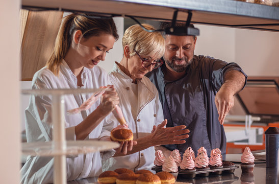 Group of workers in uniform decorating desserts in modern manufacturing.