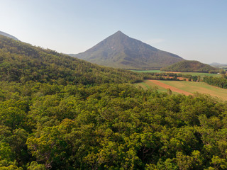 Obraz premium Beautiful mountain landscape with sugar cane fields foreground. Dramatic DRONE aerial view of fields, trees, green forest, farm, mountains, blue sky & road. Shot in Walsh's Pyramid, Cairns, Australia.