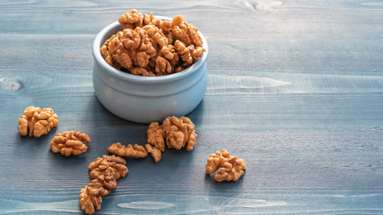 Walnuts in a blue cup on a blue wooden table.