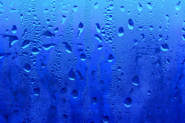 Glass with drops of water for the backdrop. Main color is classic blue. Gradient. Concept of rain, humidity.
