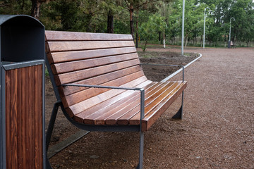New brown wooden bench and trach bin in a park with rain drops on them. Park after rain.