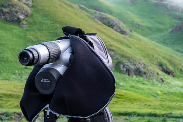 Gray spotting scope or monocular on a green mountains background.