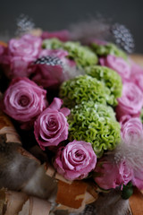 Beautiful spring bouquet close-up with pink roses and green carnations, decorated with feathers and birch bark. 