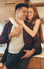Lovely caucasian girl with red hair and freckles embracing her lover while standing on the table in the kitchen