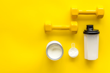 Sport nutrition. Whey protein, shaker, dumbbells on yellow background top-down flay lay copy space
