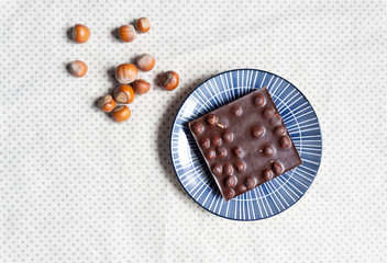 Black chocolate bar with hazelnuts  in plate on textile cover background