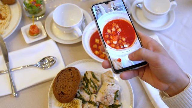 Hands using smartphone taking photos of chicken pasta with tomato coup and slice of bread