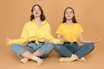 Portrait of funny cute charming ladies have meditation asana incredible zen sitting in lotus position impressed isolated dressed modern outfit on pastel background
