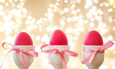 easter and holidays concept - pink colored eggs in ceramic cup holders with ribbon over festive lights on beige background