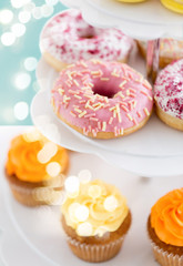 fast food, dessert and sweets concept - close up of glazed donuts and cupcakes on stand over lights on blue background
