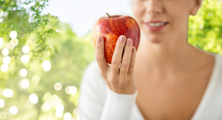 food, diet and people concept - close up of woman holding ripe red apple over green natural background