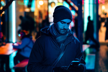 man outdoor at night in the city using a mobile phone surrounded by the neon sign lights