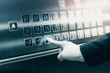 A hand wearing white disposable rubber gloves is pressing elevator button