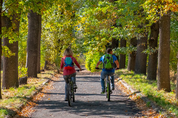 Young couple riding bicycles in autumn park.