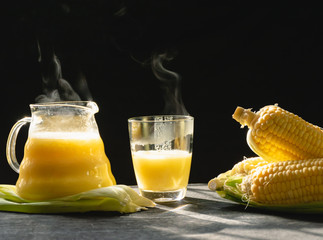 The steam from a jug and a glass of corn milk on black background, Warm drinks make good...