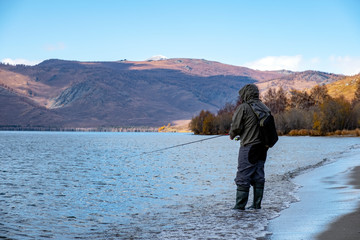 Fisherman with fiching rod on a lake in autumn. Man fisherman is catching a predator fish.