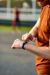Young man using hand watch during exercising / stretching in urban park.