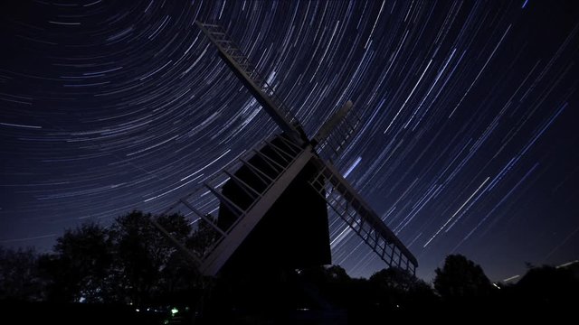 The sky spins over a windmill in Bourn, Cambridgeshire, UK. Star trail effect time-lapse shows the extent of motion in the stars.