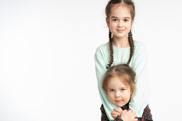 Beautiful little girls, child with pigtails hugging her little sister, both looking at the camera, isolated over white background