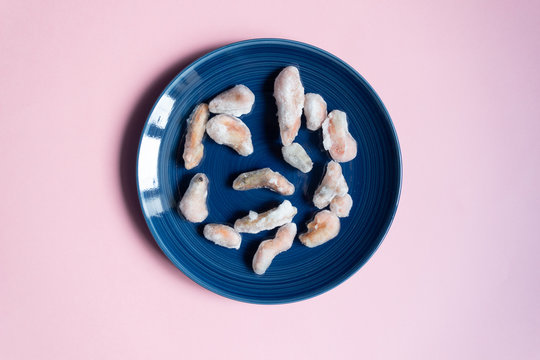Frozen shrimps in ice on blue blate on pink background