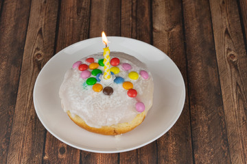 Delicious small birthday cake with one burning candle on wooden background