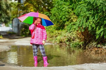 Playful little girl hiding behind colorful umbrella outdoors