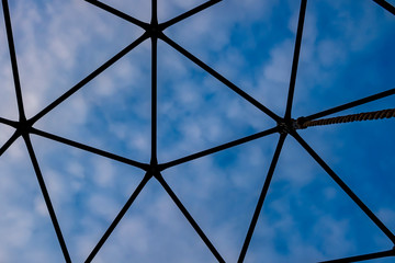 Part of geodesic dome construction with cloudy blue sky background.
