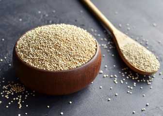 Organic quinoa grains in wooden bowl and spoon on black concrete background