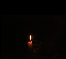 Small lighted candle in a glass with black background, wide shot