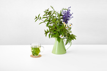 eco and organic concept - herbal tea and flowers in green jug on on white background