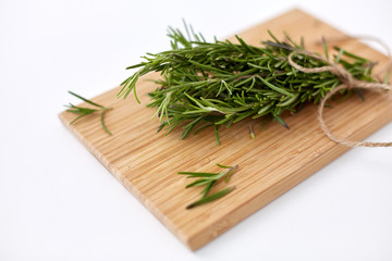 greens, culinary and ethnoscience concept - bunch of rosemary on wooden cutting board