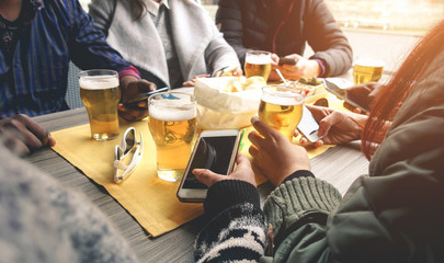 Young people drinking beers in pub restaurant patio while using cell mobile phones - Frindship,...