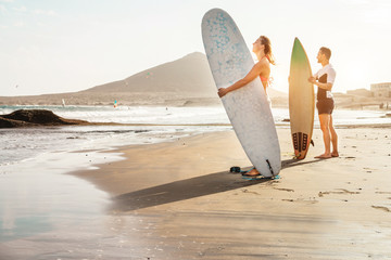 Surfers couple waiting for the high waves on beach - Sporty people with surf boards at sunset - Extreme sport and vacation concept - Focus on female face