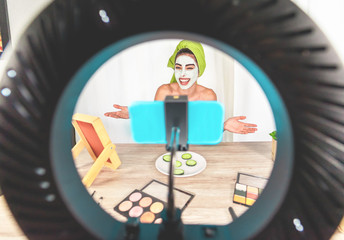 Happy influencer girl having fun creating videos using beauty skincare mask - Young woman streaming...