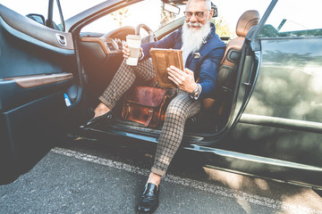 Hipster stylish man using tablet sitting inside convertible electric car - Senior entrepreneur...