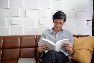 Naklejka premium Senior Asian man reading book on sofa in living room at home ,Portrait of Asian elderly man is Relaxing and Happiness With Read a Magazine
