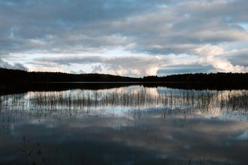 Beautiful lake with still water, reflections of clouds on surface and trees silhouettes.