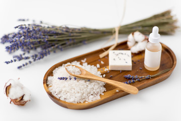 beauty and wellness concept - sea salt with spoon, soap, serum with dropper, lavender and cotton flowers on wooden tray