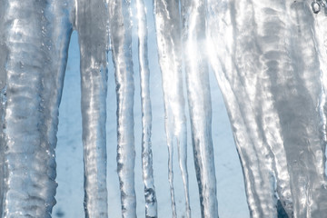 Icicles hanging down from a roof with clear blue sky and sun on a background.