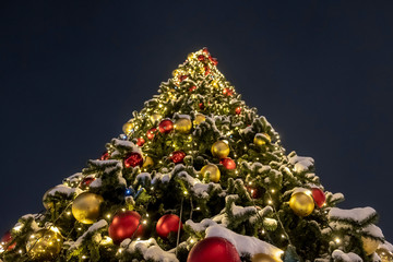 City street outdoor decorated Christmas tree in perspective with red and golden baubles and garlands at night.