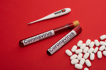  Pills, thermometer and test tubes with blood samples and coronavirus lettering on red surface