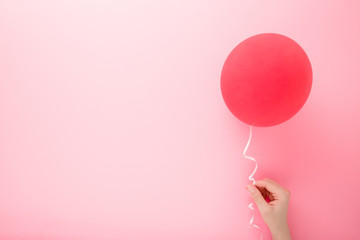 Young woman hand holding one red balloon on light pink background. Pastel color. Empty place for...