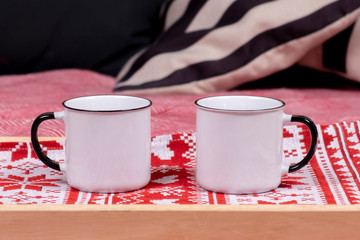 Tray with two metal cups on the bed with pillows and garland background. Winter holidays. Breakfast time.
