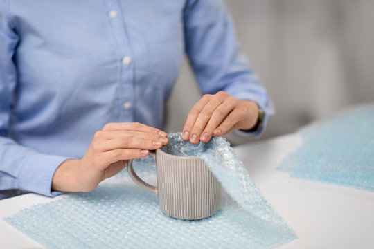 Delivery, Mail Service, People And Shipment Concept - Close Up Of Woman Packing Mug And It Wrapping Into Protective Bubble Wrap At Post Office