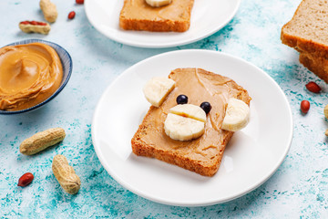 Funny bear and monkey face sandwich with peanut butter, banana and black currant on light background,top view