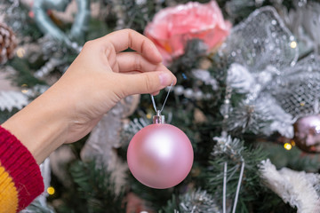 Close-up of a female hand decorating christmas tree with toys. Christmas and New Year holidays.