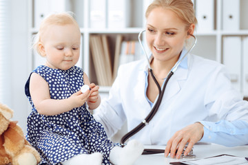 Doctor and patient in hospital. Little girl dressed in dark blue dress in peas is being examined by doctor with stethoscope. Medicine concept