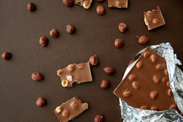 sweets, confectionery and food concept - milk chocolate bar with hazelnuts in foil wrapper on brown background